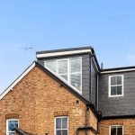 Modern loft conversion on a brick house with black slate siding and large windows.
