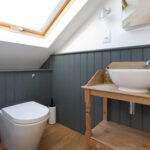 Modern loft conversion bathroom with skylight, featuring toilet and wooden sink unit.