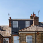 Loft conversion on a brick terraced house, enhancing space and adding value. Blue sky background.