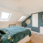 Modern loft conversion bedroom with skylights, green walls, and cozy decor, perfect for maximizing space and light.