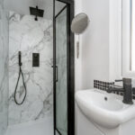 Modern loft conversion bathroom with sleek shower and sink, featuring marble wall and black fixtures.