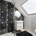 Modern loft conversion bathroom with skylight, stylish black hexagonal tiles, and glass shower.