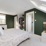 Modern loft conversion bedroom with green walls, natural light, and stylish decor. Ideal space for maximizing home value.
