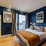 Modern loft conversion bedroom with blue walls, wooden floors, and large window for natural light. Cozy and stylish design.