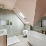Modern loft bathroom with skylight, green tiles, freestanding tub, and glass shower. Ideal for loft conversions.