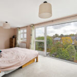 Bright and airy converted loft bedroom with garden view, featuring a large window and modern decor. Perfect for relaxation.