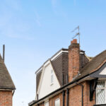 Loft conversion with new dormer window and roofing on a traditional home against a clear blue sky.