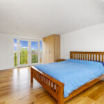 Modern loft conversion bedroom with wooden flooring, blue bedding, and balcony view. Bright and spacious design.