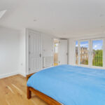 Modern loft conversion with large windows, blue bedding, and wooden flooring. Bright, airy, and spacious bedroom design.
