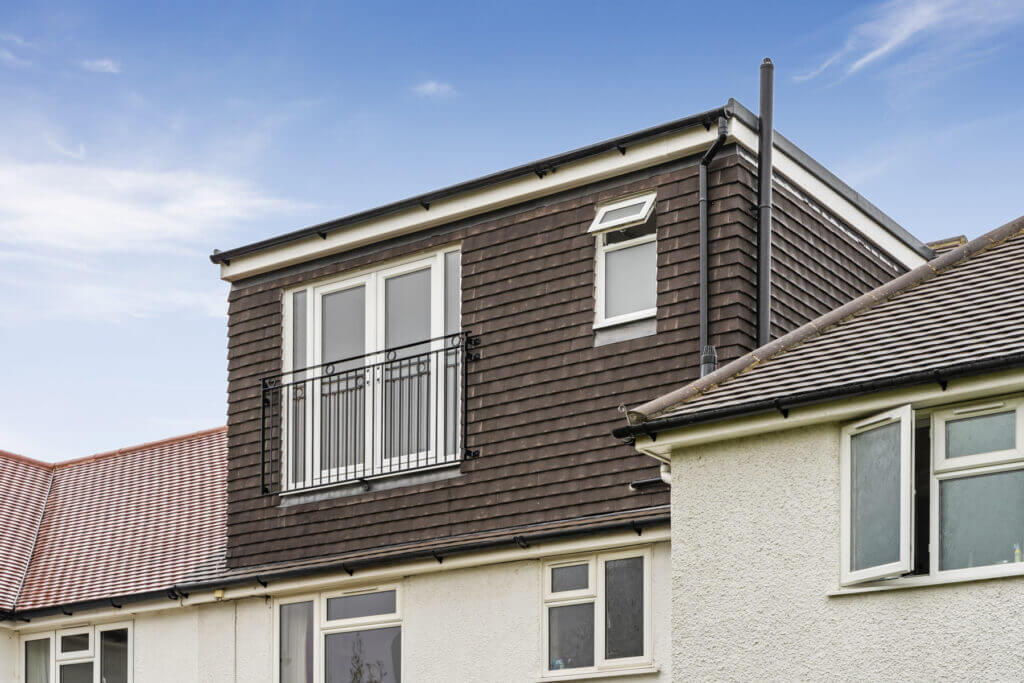 Modern loft conversion with balcony on residential home under clear blue sky.