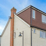 Dormer loft conversion on a sloped roof with large windows under a clear blue sky.