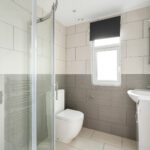Modern loft conversion bathroom with grey tiles and glass shower enclosure.