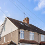 Modern loft conversion on a semi-detached house with skylights and a textured finish, under a clear blue sky.