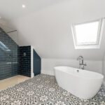 Modern loft conversion bathroom with freestanding tub, skylight, and patterned tiles. Efficient use of attic space.