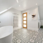 Modern loft conversion bathroom with elegant bathtub, patterned floor tiles, and wall art. Bright and spacious design.