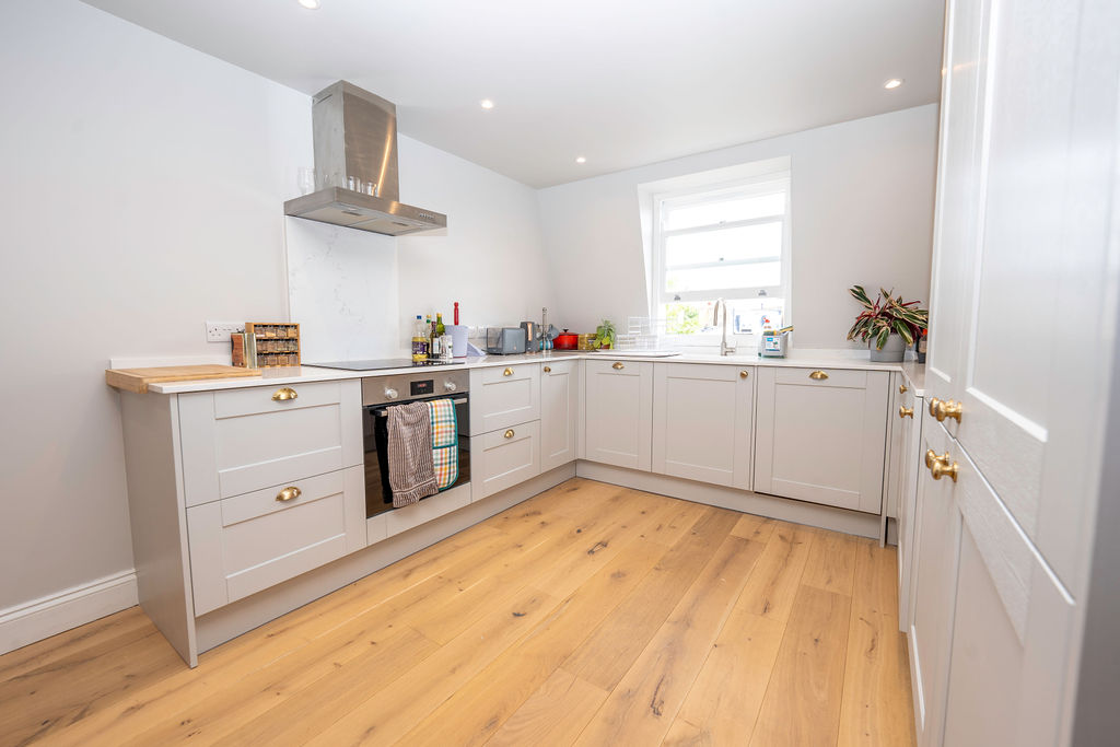 Modern loft conversion kitchen with white cabinets, wood floors, and natural light from window.