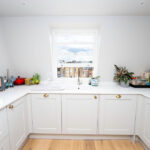 Modern loft conversion kitchen with sleek white cabinets and city view through skylight window.