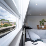 Modern loft conversion with cozy living area and large window offering a scenic view of the neighborhood.