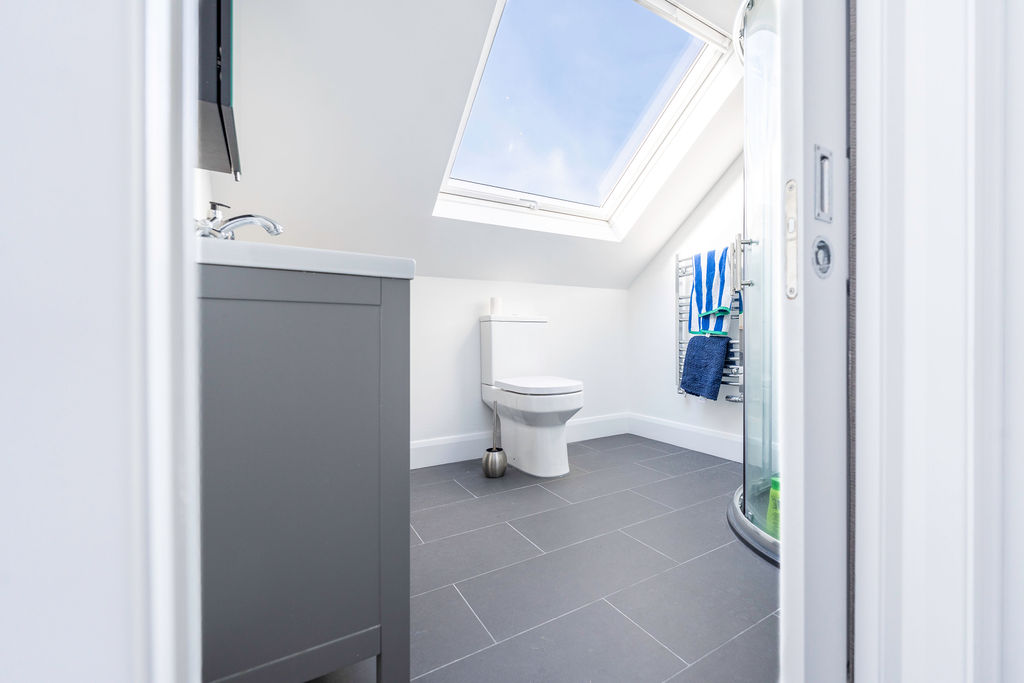 Modern loft conversion bathroom with skylight, grey tiles, and compact design for optimized space and natural light.