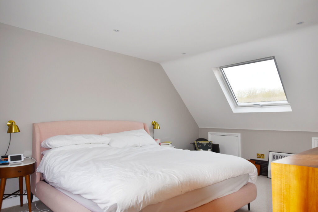 Bright loft conversion bedroom with skylight, modern decor, and cozy bed. Ideal use of attic space for comfort.